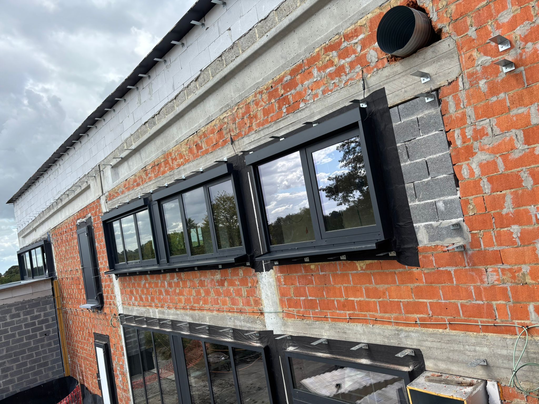 Bandes vitrées anthracite vues en angle sur une façade en briques en chantier