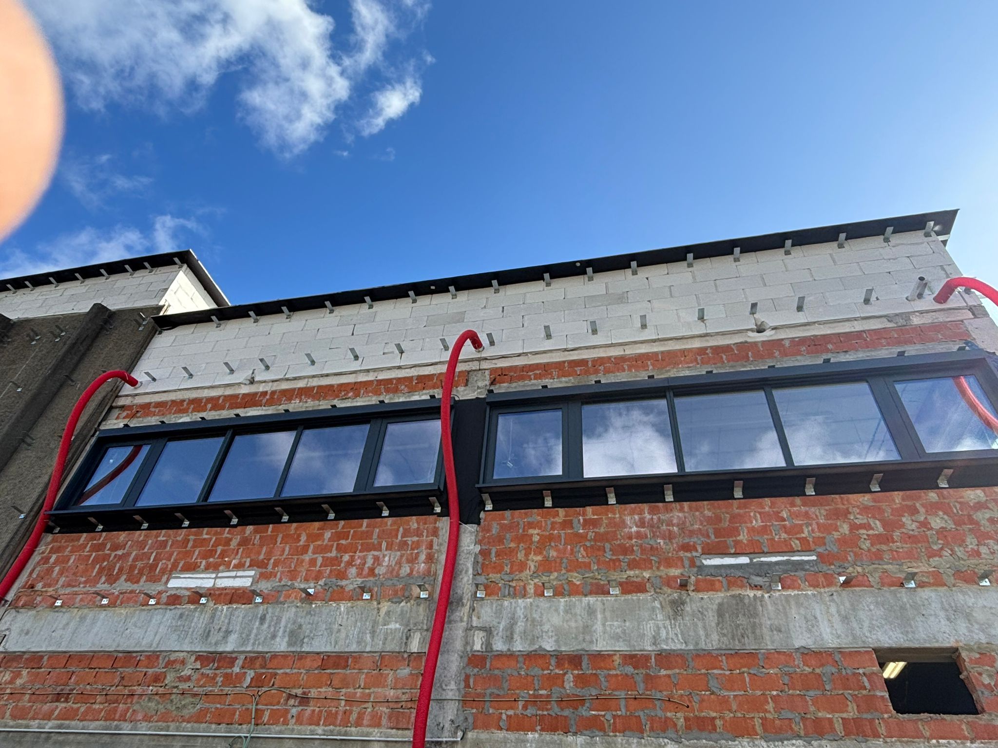 Bande vitrée continue sous ciel bleu, façade en cours d’isolation