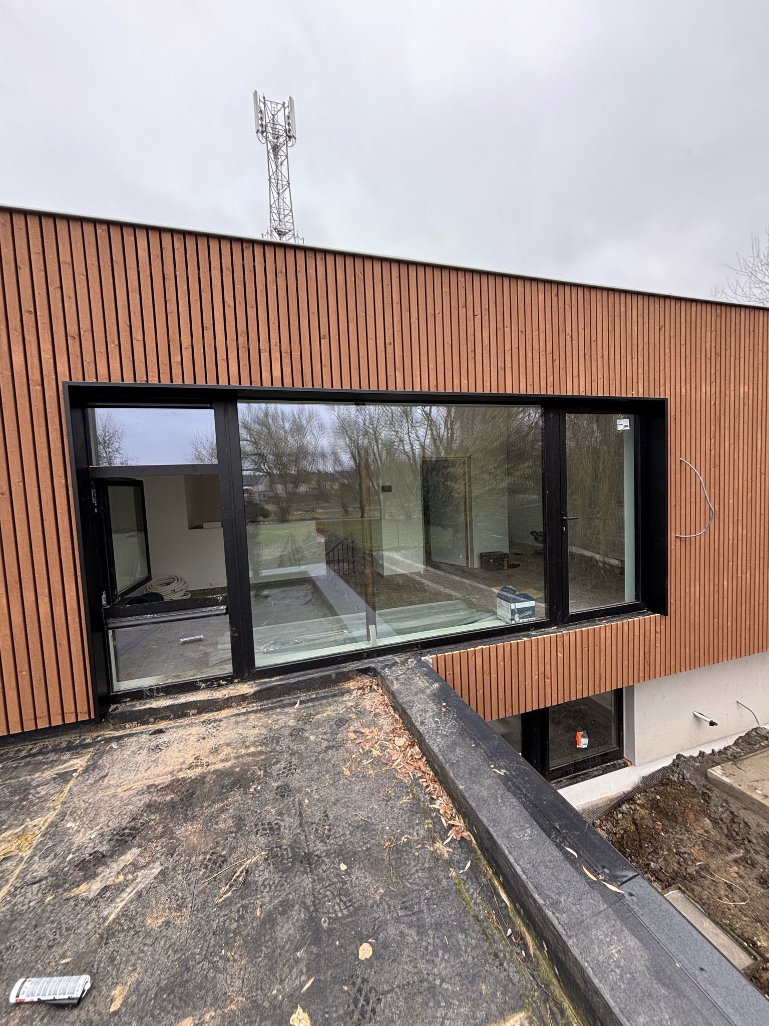 Grande baie vitrée anthracite encastrée dans une façade en bardage bois vertical