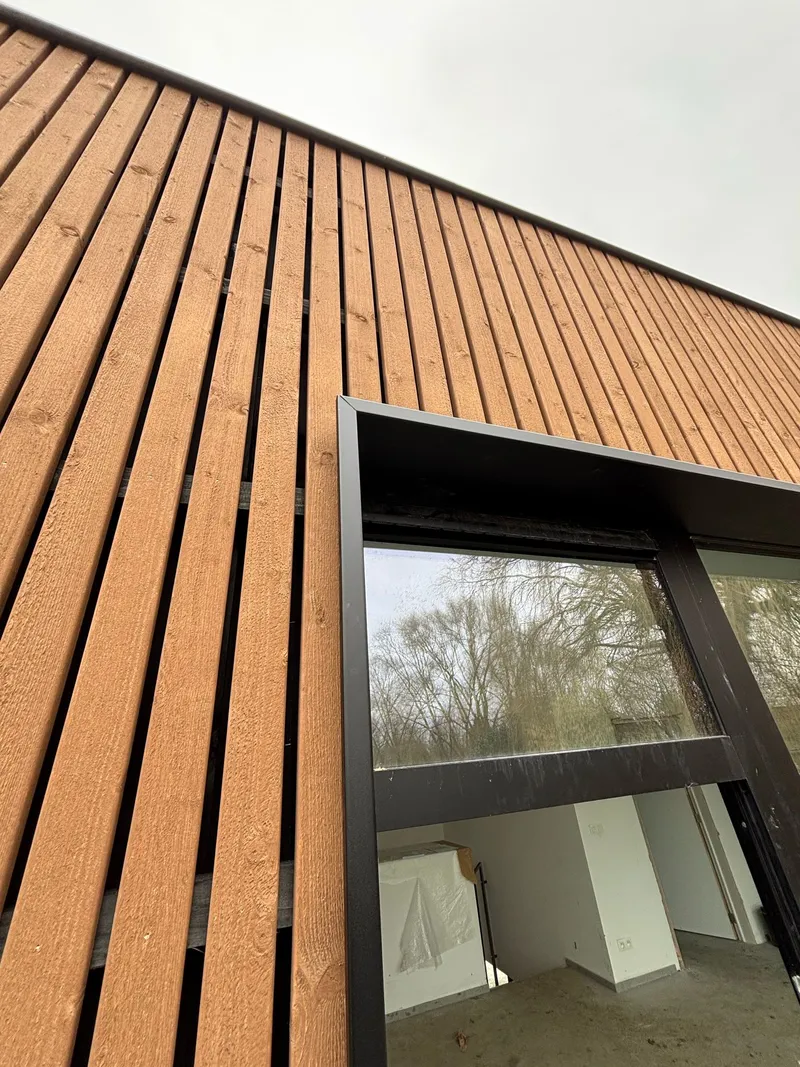 Détail en contre-plongée du raccord entre châssis anthracite et bardage bois