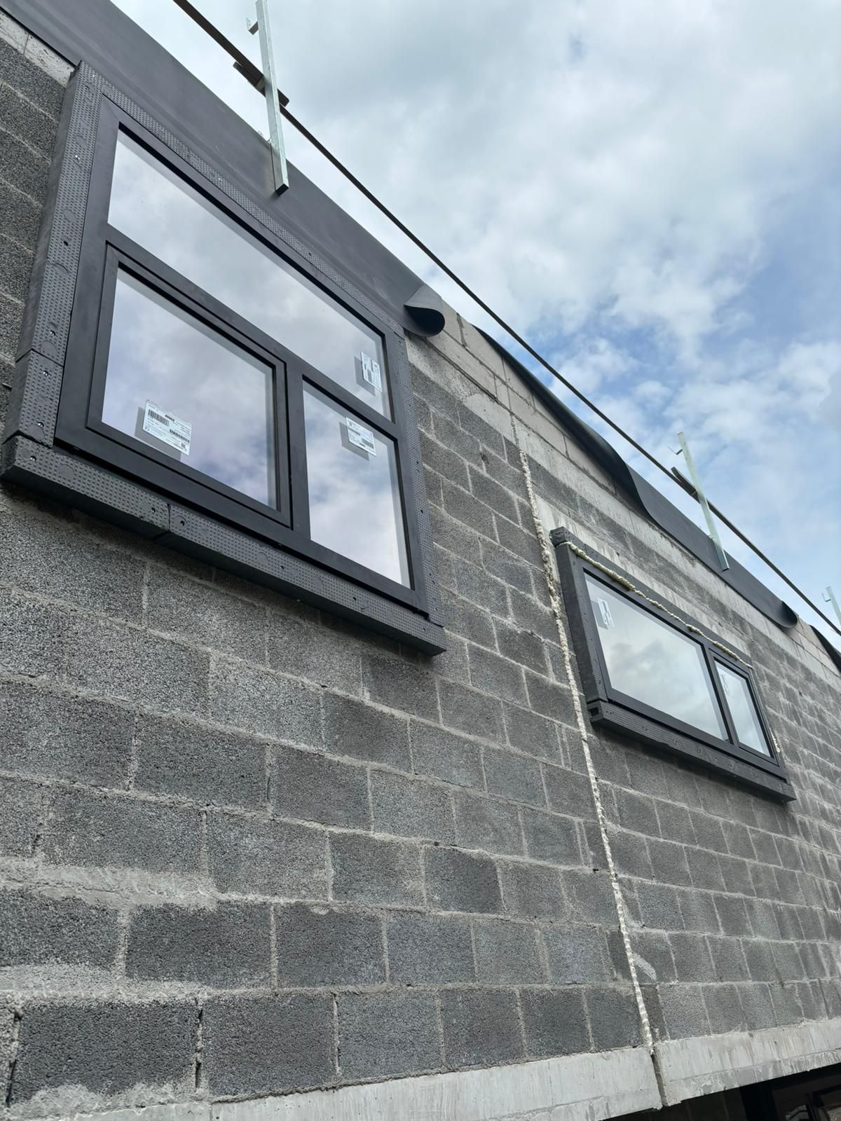 Construction en blocs avec deux fenêtres noires posées, isolation de toiture en cours