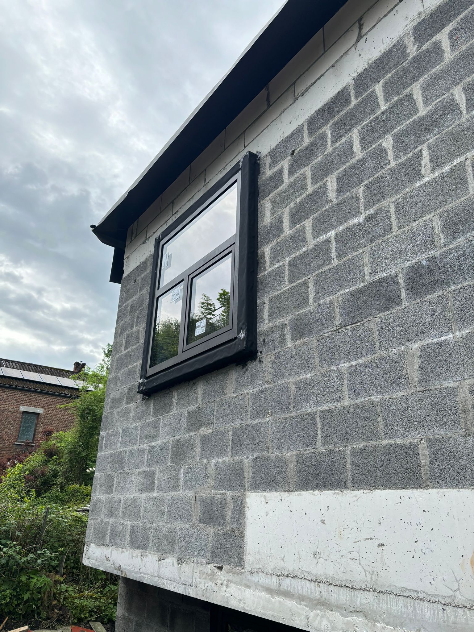 Fenêtre noire posée dans un pignon en blocs, chantier au stade gros œuvre fermé