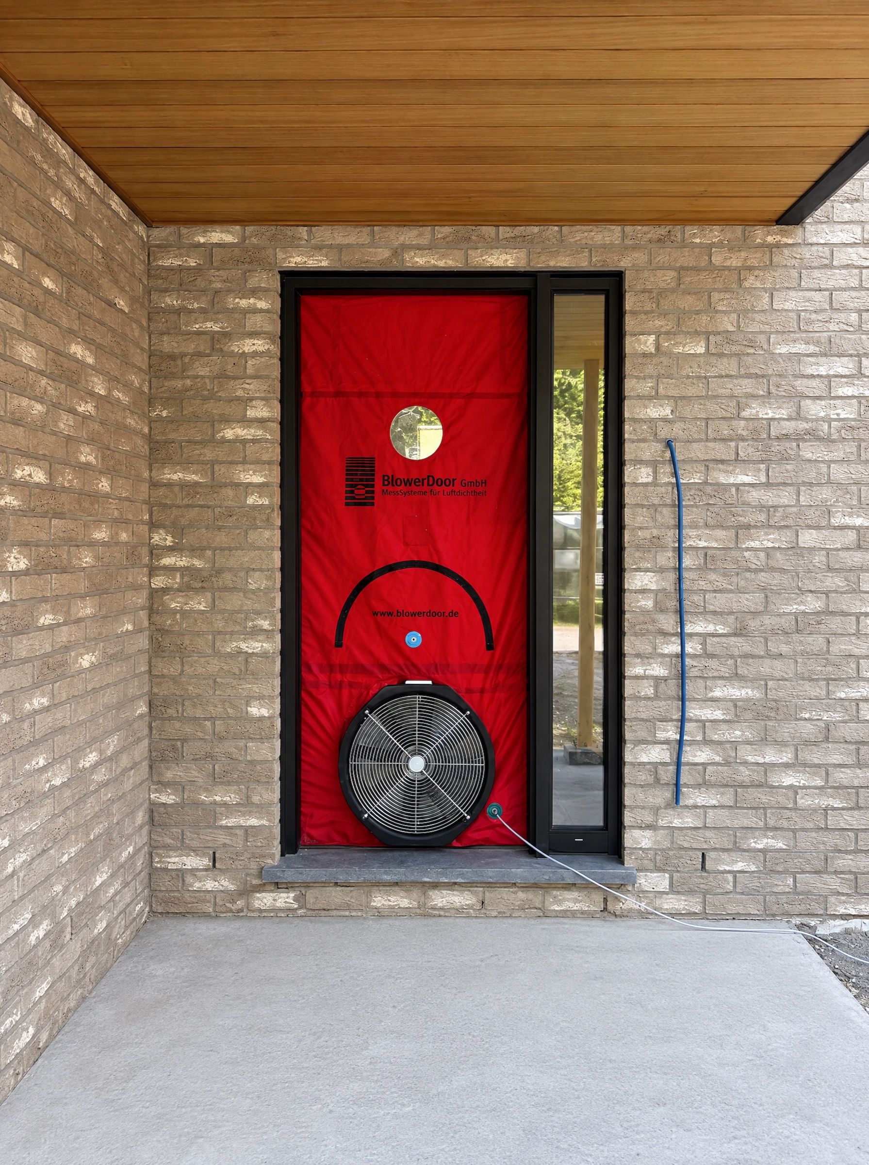 Toile rouge de test blower door et ventilateur montés dans une porte d’entrée en briques claires