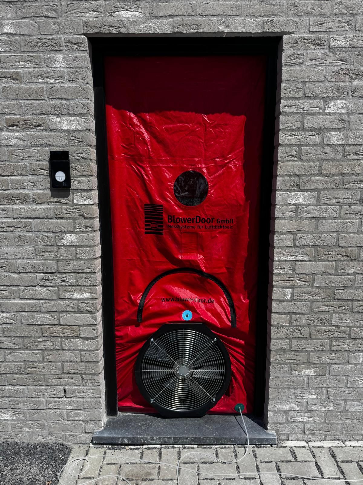 Ventilateur de mesure monté dans la porte d’une maison en briques grises
