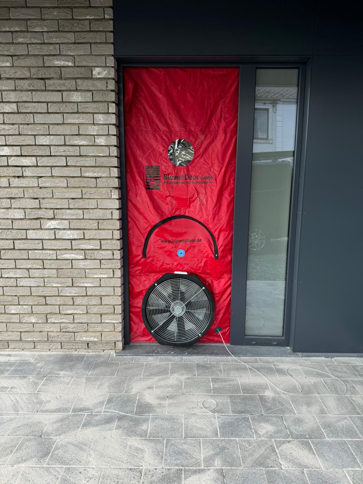 Test blower door sur une porte d’entrée entre briques grises et panneau sombre